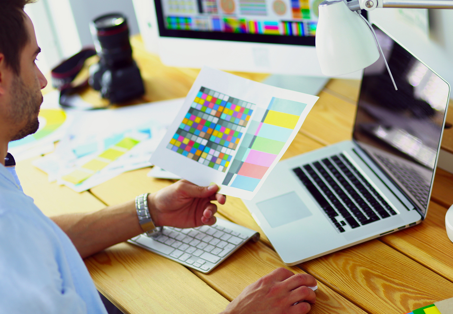Portrait of young designer sitting at graphic studio in front of laptop and computer while working online.